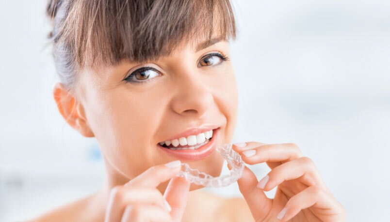 A woman smiling while holding a bruxism night guard