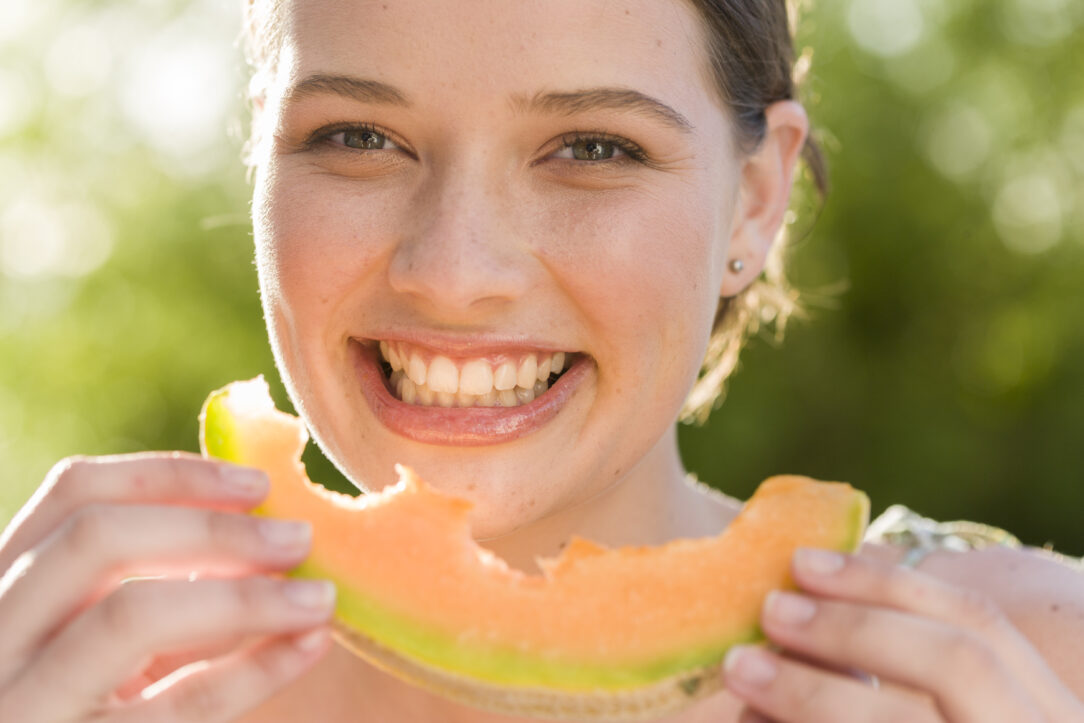 portrait-smiling-woman-eating-melon-outdoors